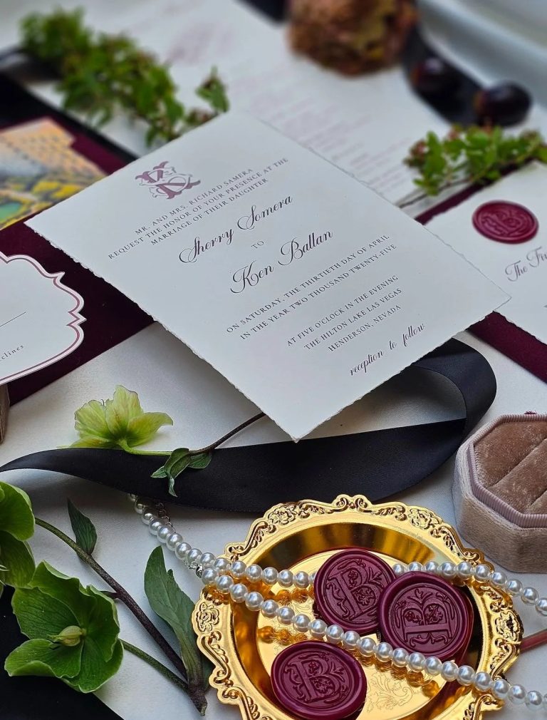 Wedding invitation suite with burgundy accents and wax seals styled among flowers.