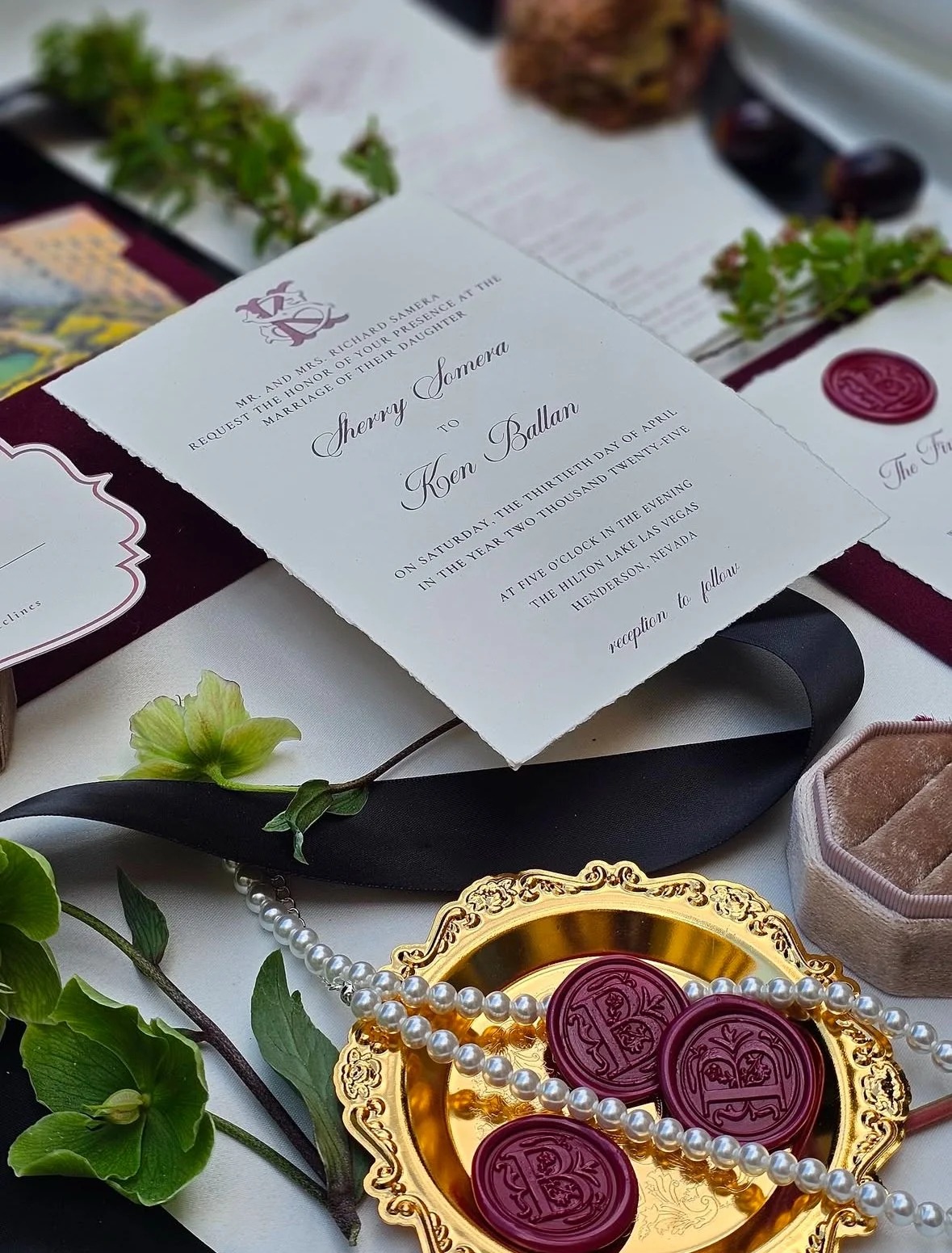 Wedding invitation suite with burgundy accents and wax seals styled among flowers.