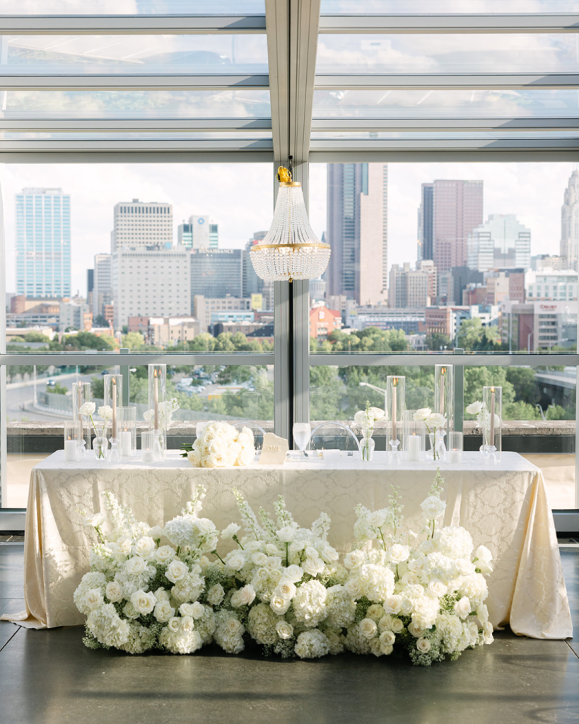 White floral sweetheart table with champagne linen, glass candles and panoramic Columbus skyline views at Revery.
