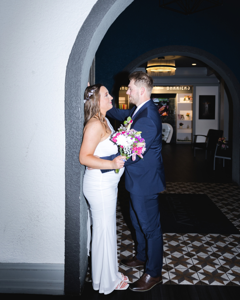 bride and groom standing in arched entryway of The Aviator with a colorful bouquet