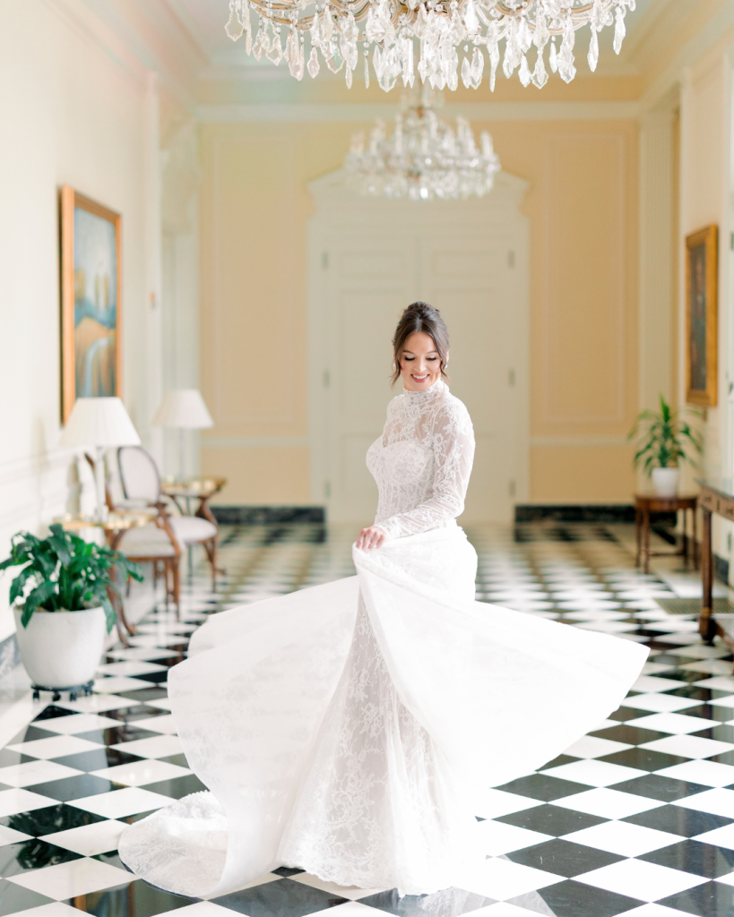 Hannah twirls in her lace wedding gown on a black and white checkered floor beneath crystal chandeliers.
