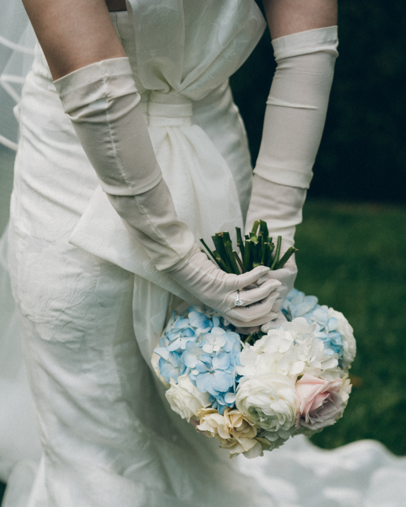 bride in sheer gloves with low back dress. gloves behind back holding wedding bouquet