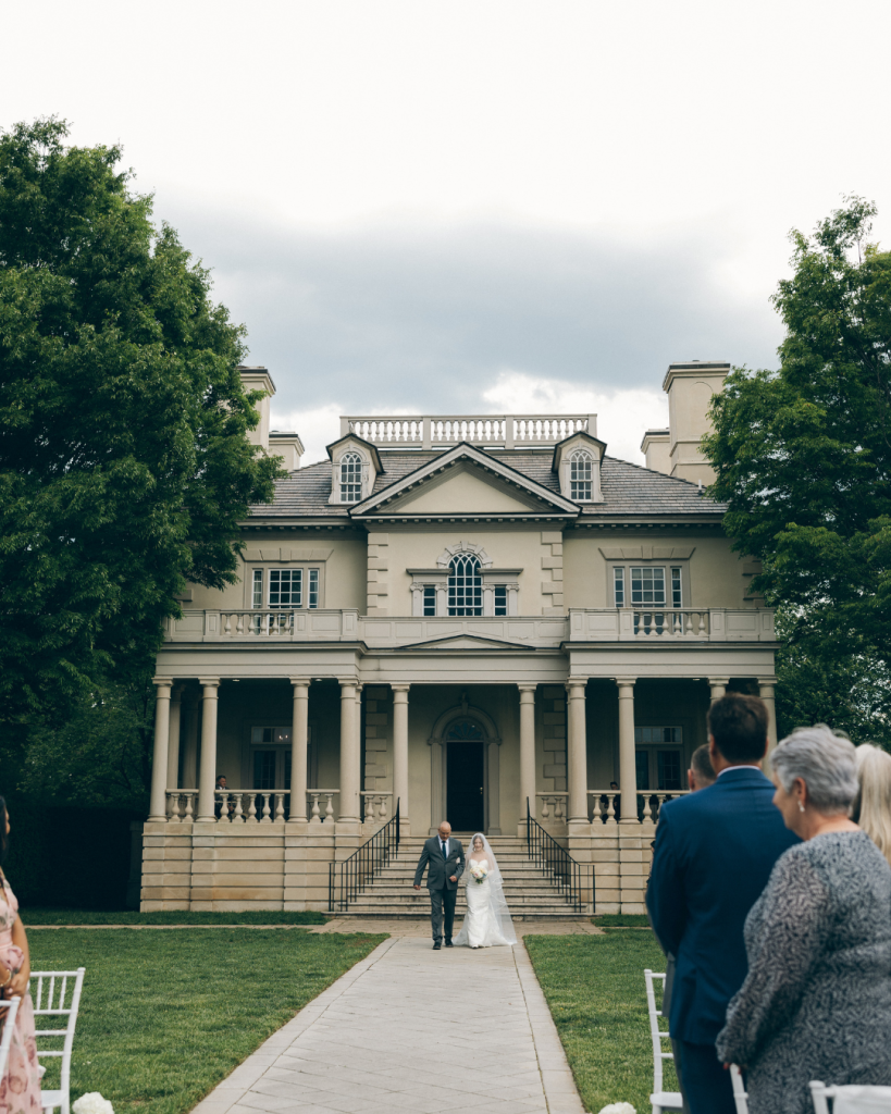 bride walking out of estate manor to wedding ceremony outdoors upscale wedding