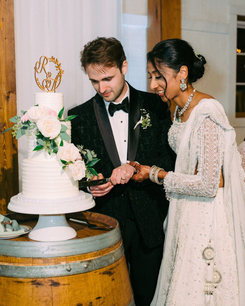 bride and groom cutting wedding cake, bride wearing whitethe South Asian silhouette, and Andrew wore a South Asian-inspired tuxedo that we got made in India,