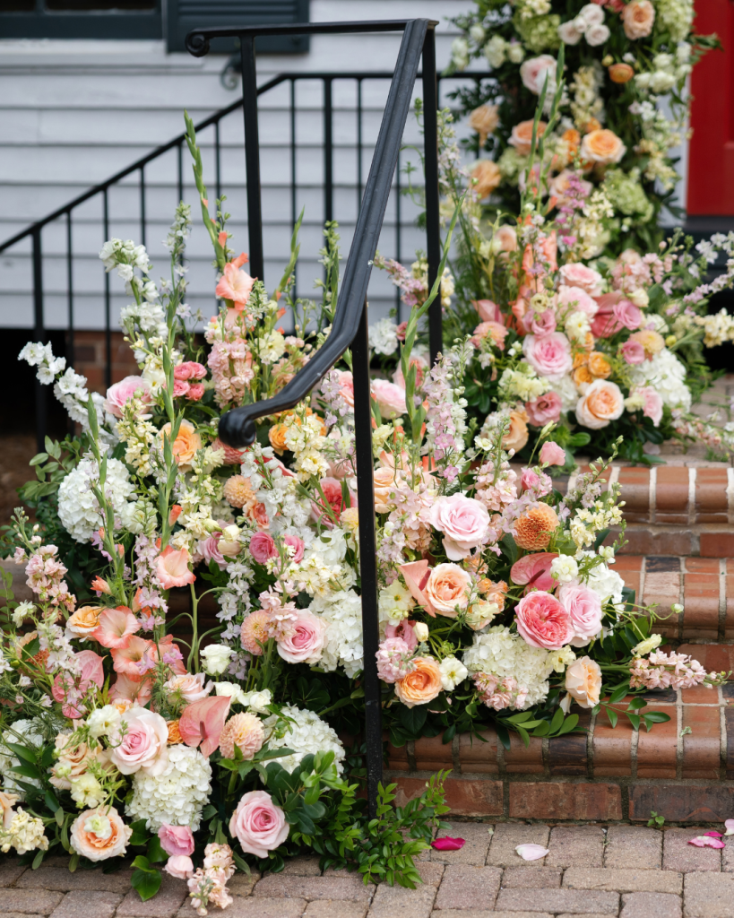 Colorful wedding florals in shades of pink, peach, yellow and white cascade along the brick steps outside the Chapel at Morning Star.