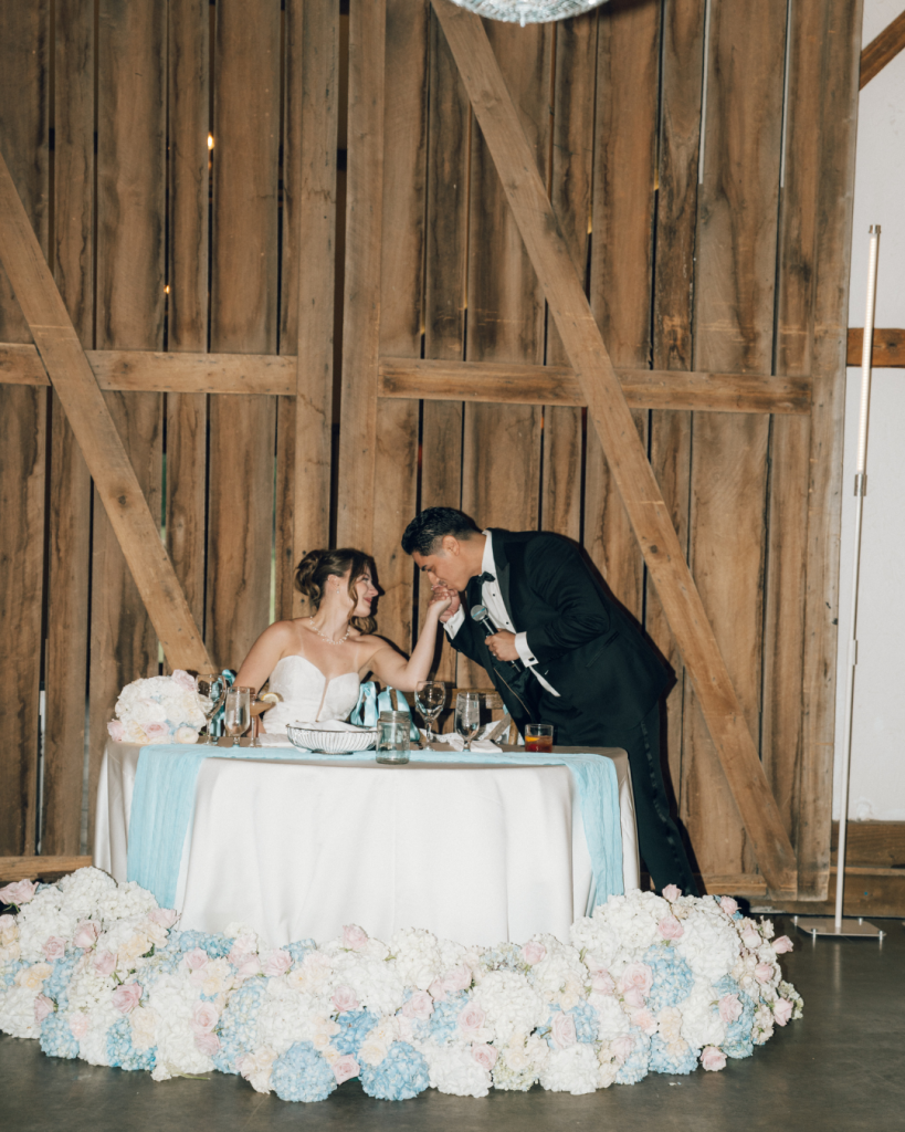 groom kissing brides hand at wedding reception at sweetheart table