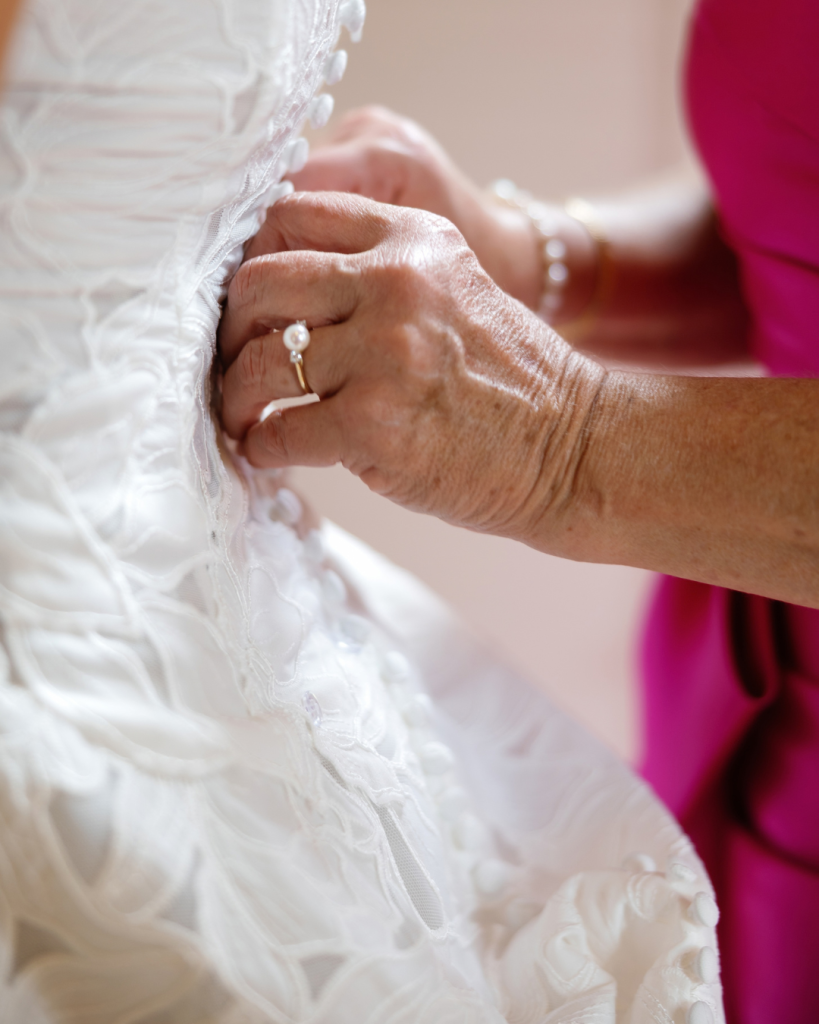 Close up of Lauren’s floral lace wedding gown being buttoned as she gets ready for her wedding day.