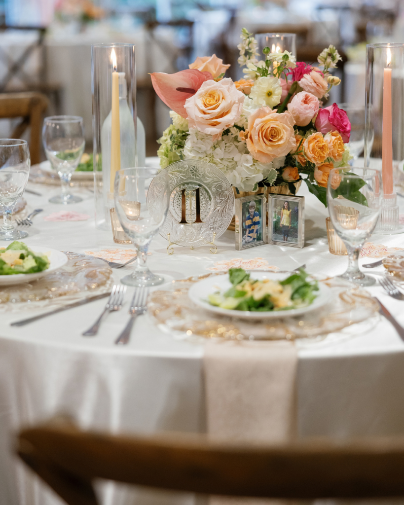 Elegant wedding reception table at Pine Lake Country Club featuring colorful florals, candlelight, layered place settings and personal childhood photos.