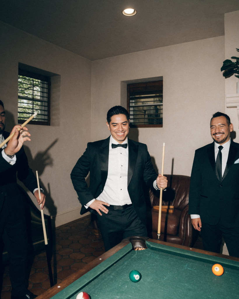 groom and groomsmen playing pool before wedding ceremony in black tux