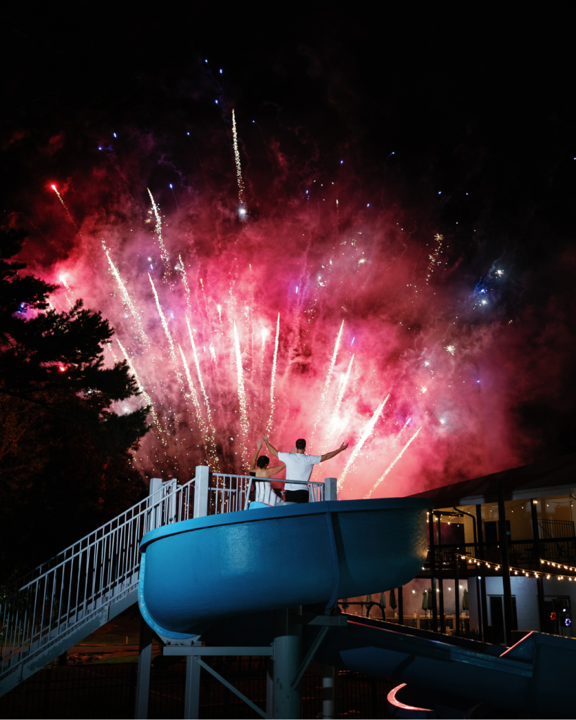 Lauren and Peyton watch a colorful fireworks display from the pool slide during their Pine Lake Country Club wedding celebration.