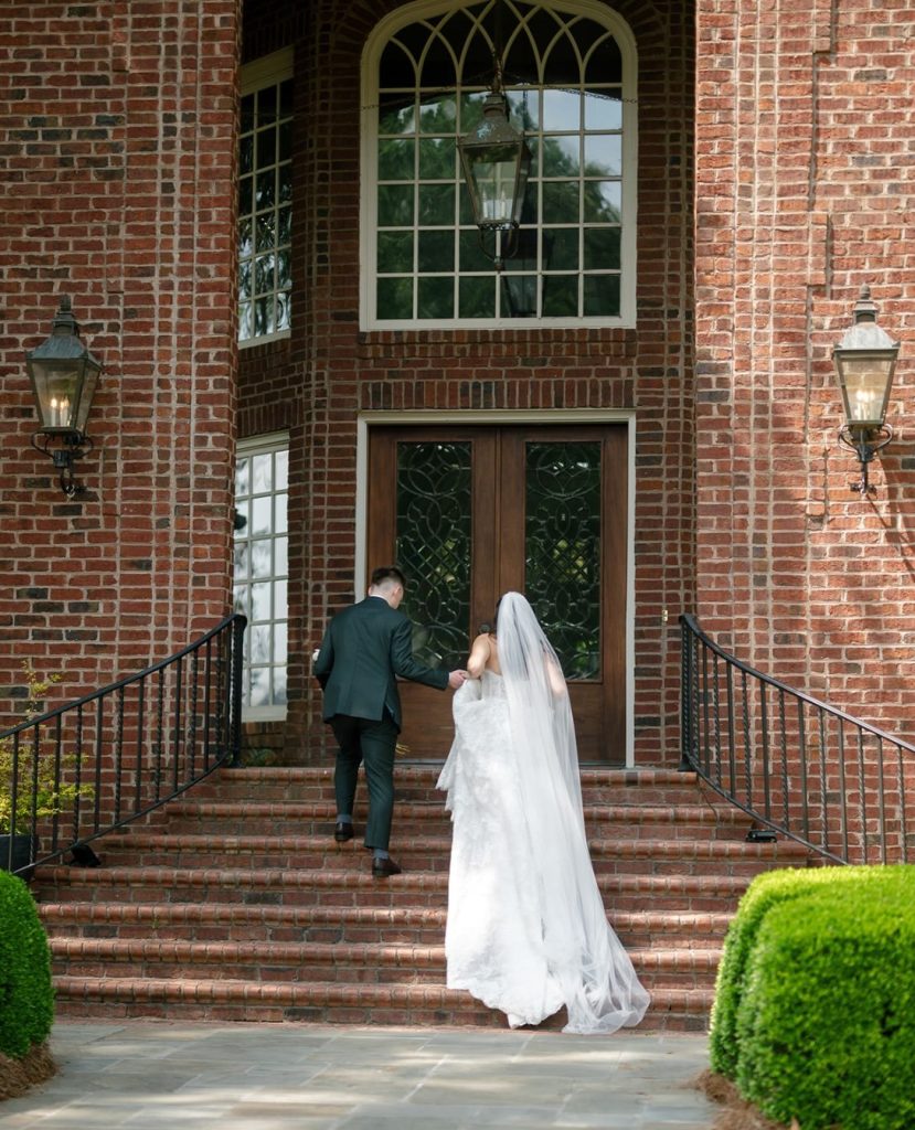 Bride and her father walking up brick steps toward the entrance of a brick venue with arched windows
