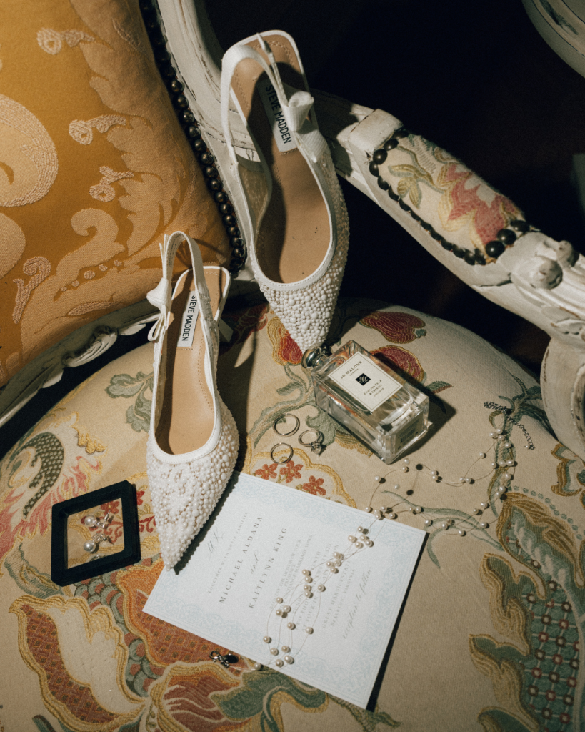 wedding details photo on golden chair with wedding invitations, slingback shoes and jewelry