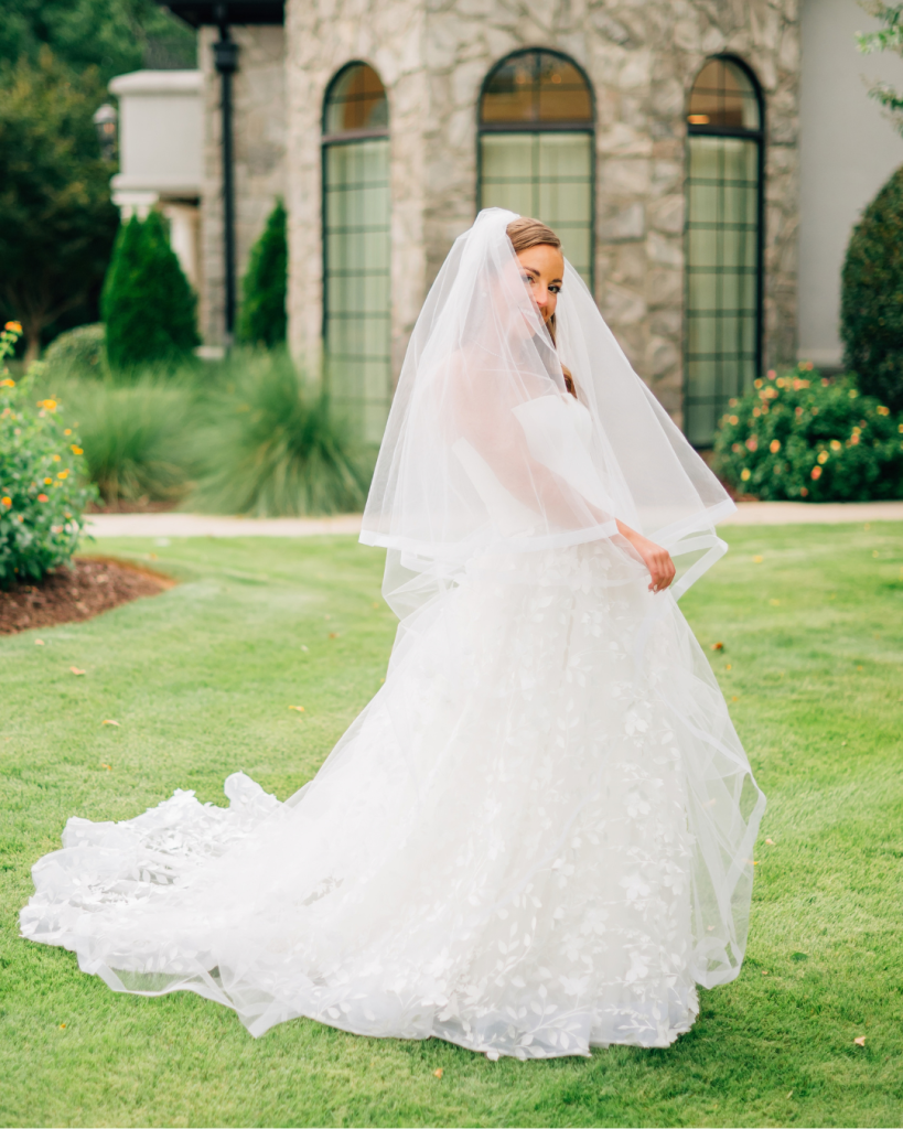 Bride Kelly poses outside Riverwalk Event Venue wearing a strapless wedding gown with dimensional floral appliqué and a soft veil.