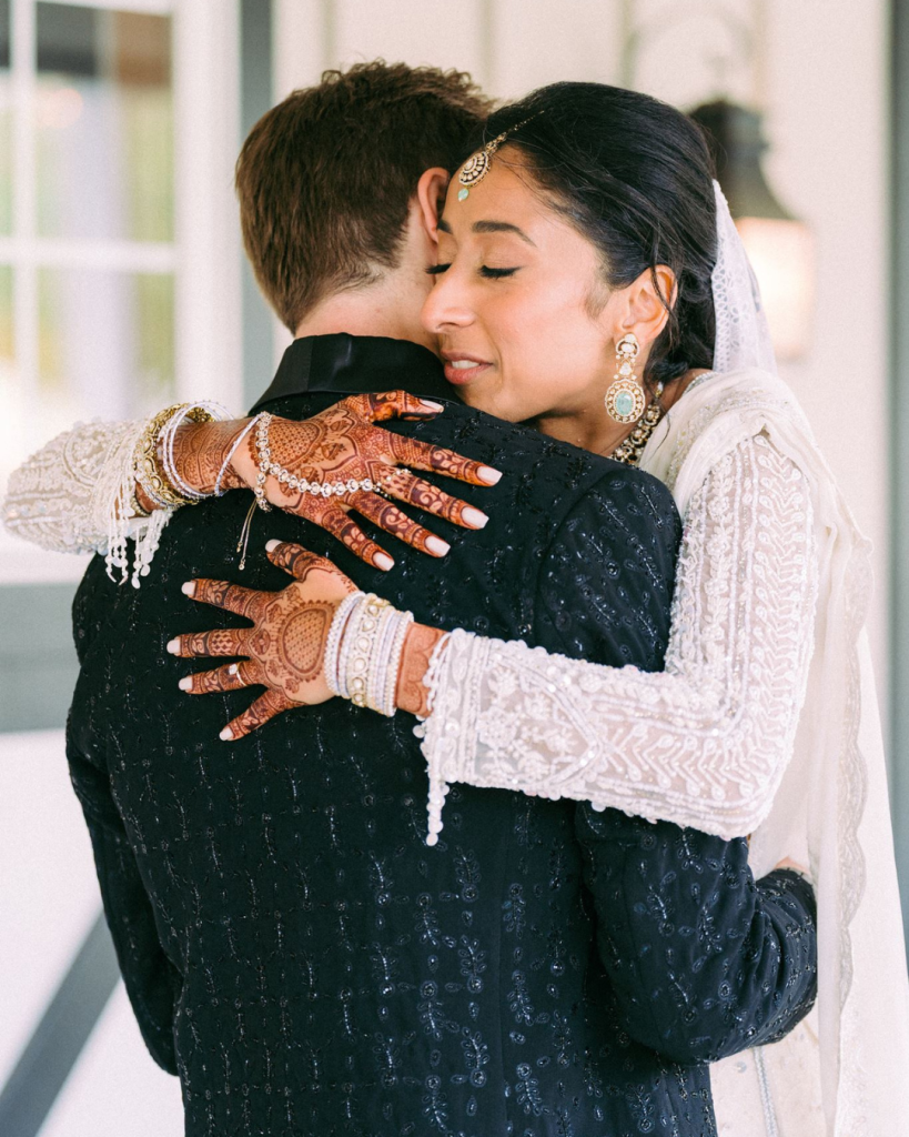 bride and groom hugging at first look. groom in sparkly black tux and bride in white south asian style dress