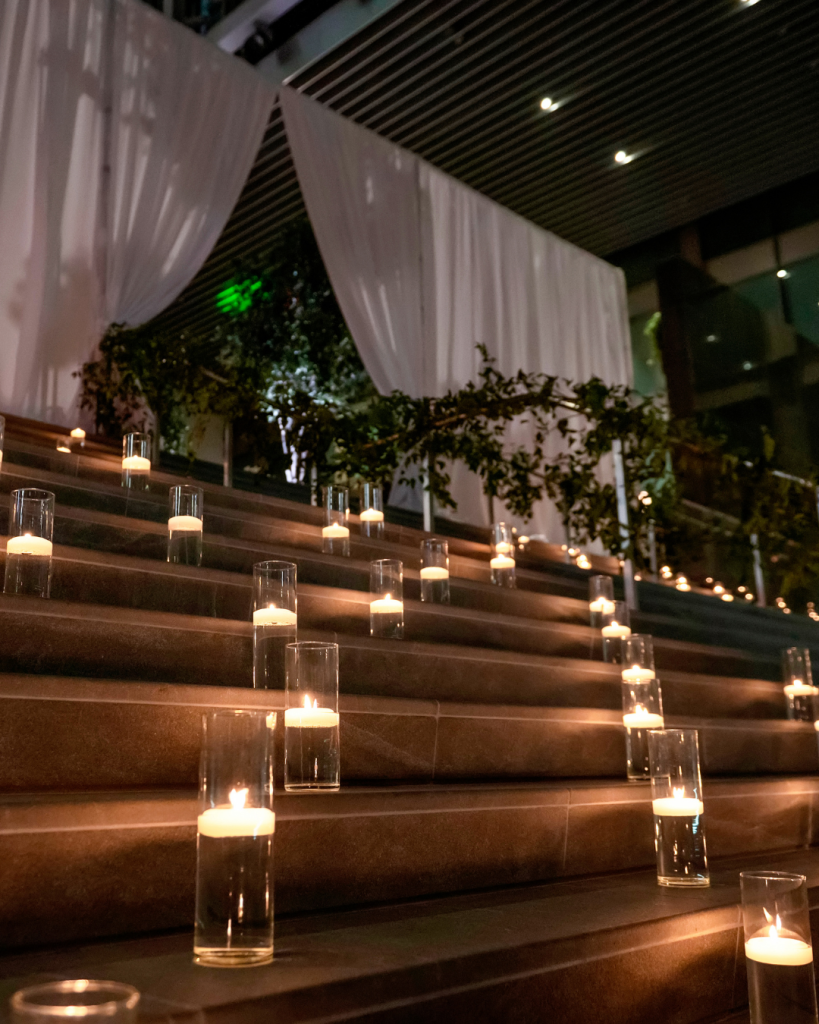 Glass cylinder candles line the wide staircase at The Ritz Carlton Charlotte beneath white draping and greenery.