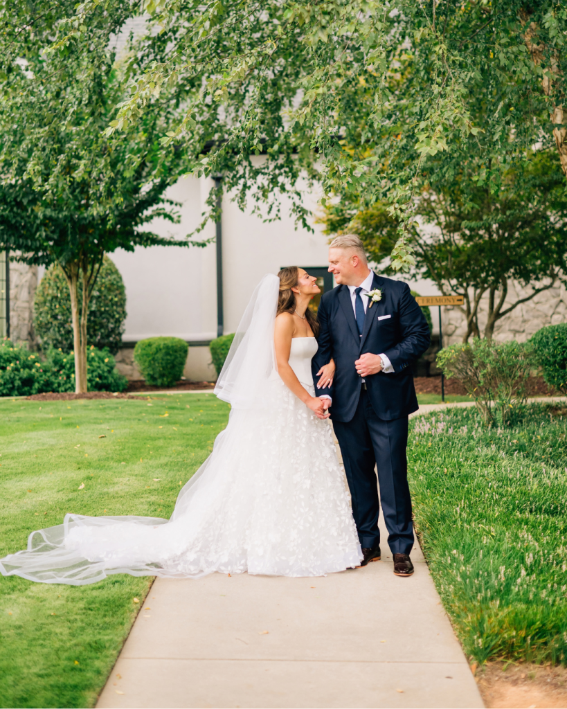 Kelly and Jason walk hand in hand through the landscaped grounds of Riverwalk Event Venue following their outdoor wedding ceremony.