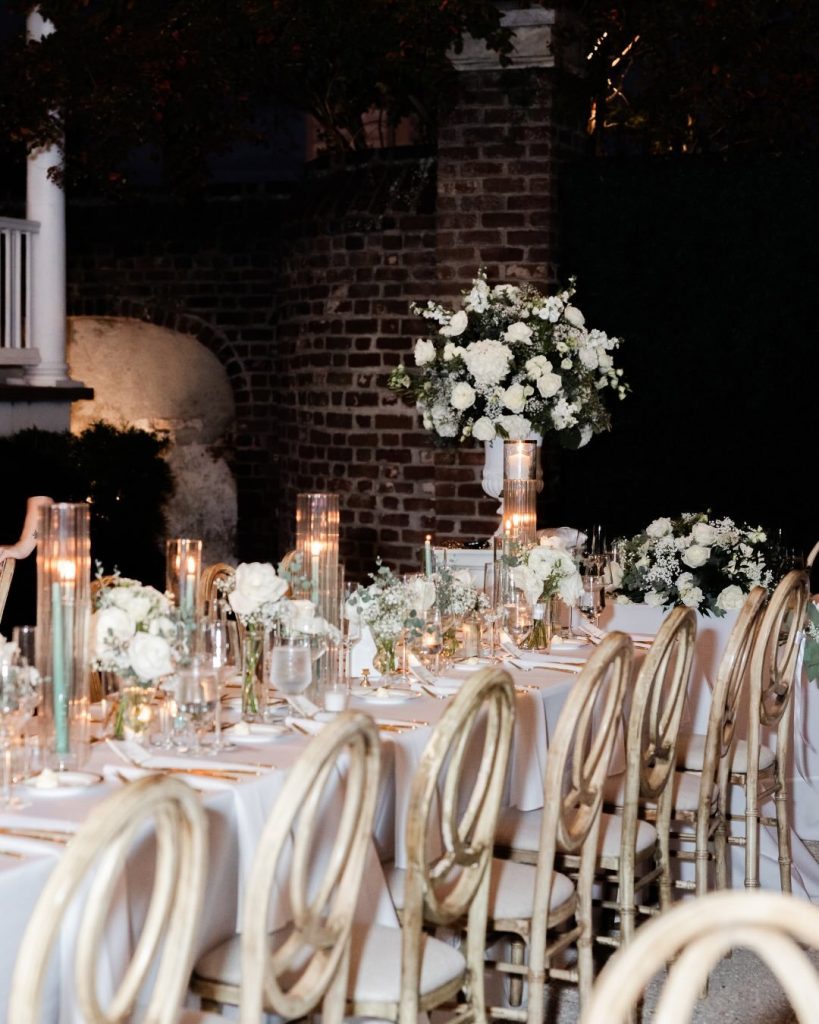 Candlelit reception table with white floral centerpieces and gold chairs at a Charleston wedding reception