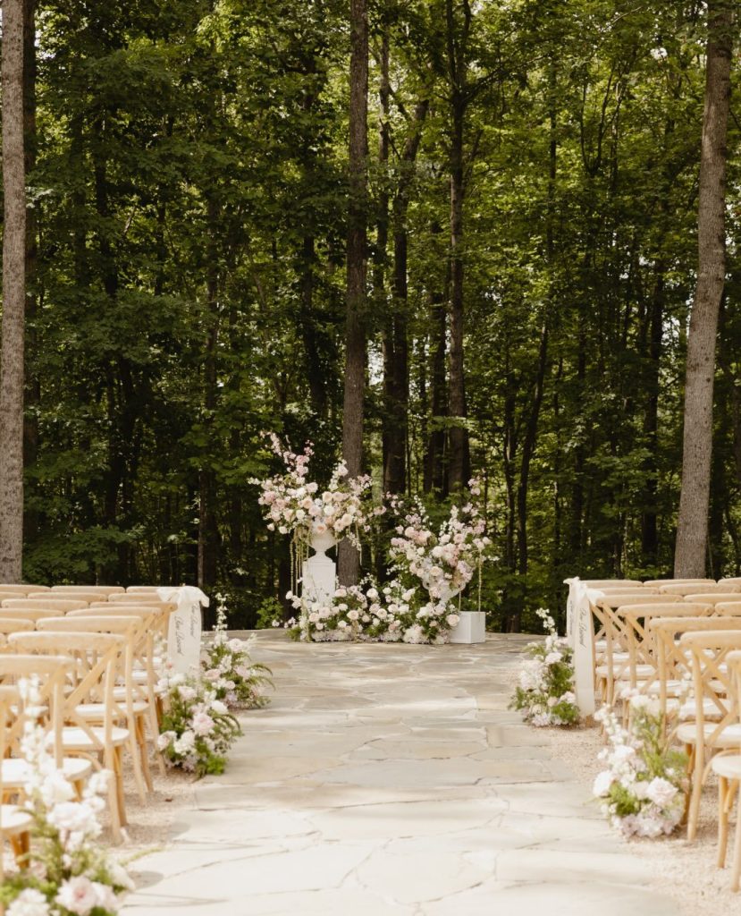 Cover 1: Outdoor wedding ceremony aisle lined with wooden chairs and a floral arch, framed by trees