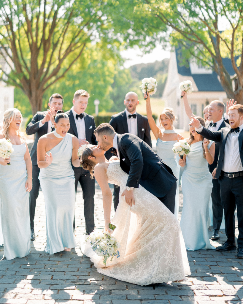 Hannah and Johnathan celebrate with their wedding party dressed in soft blue bridesmaid dresses and black suits.