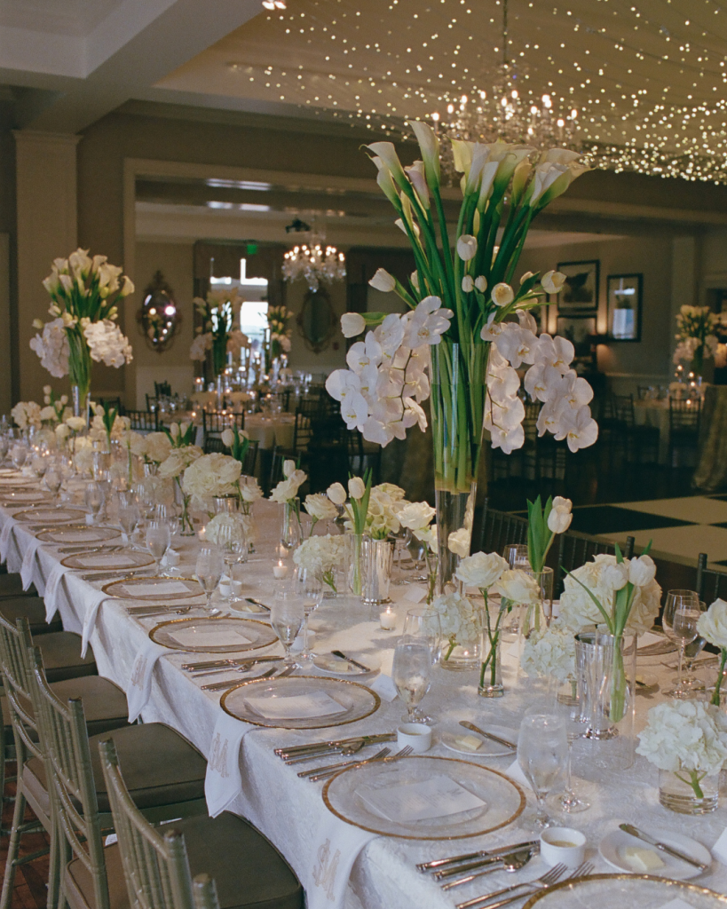 Long reception table with white floral centerpieces by Watered Garden Florist at a Carolina Country Club wedding in Raleigh NC