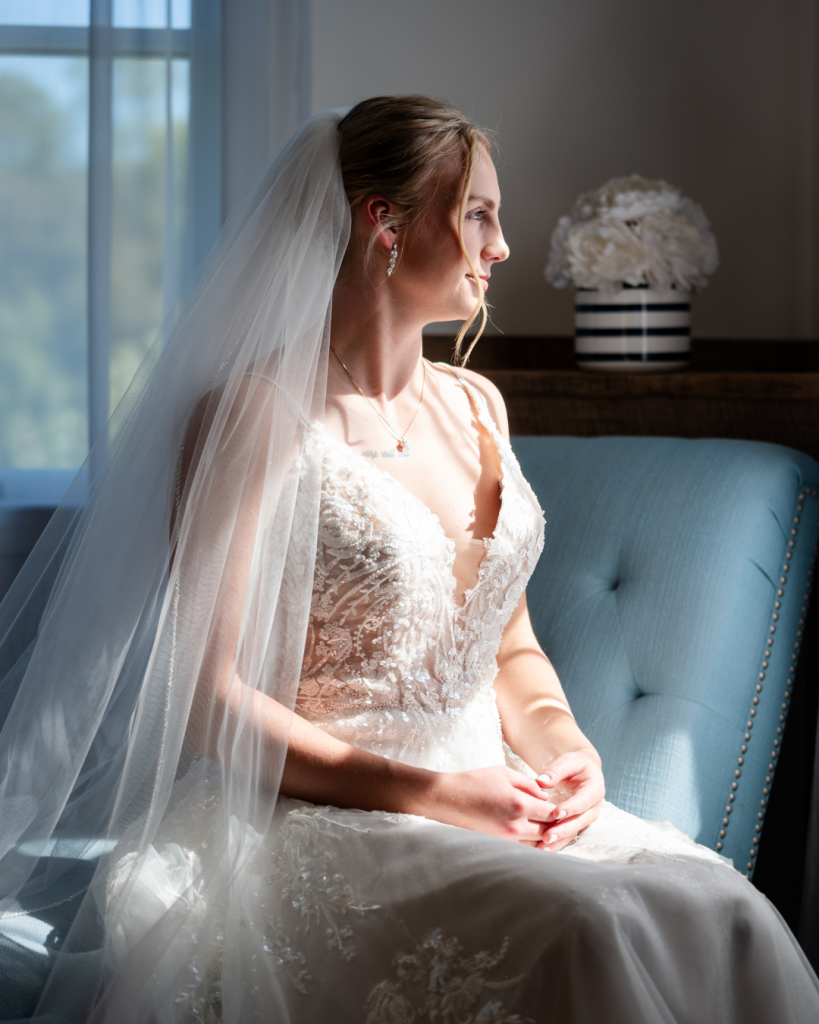 Bride seated beside a window in a lace wedding gown and long veil during an October wedding in Elkton, Maryland.