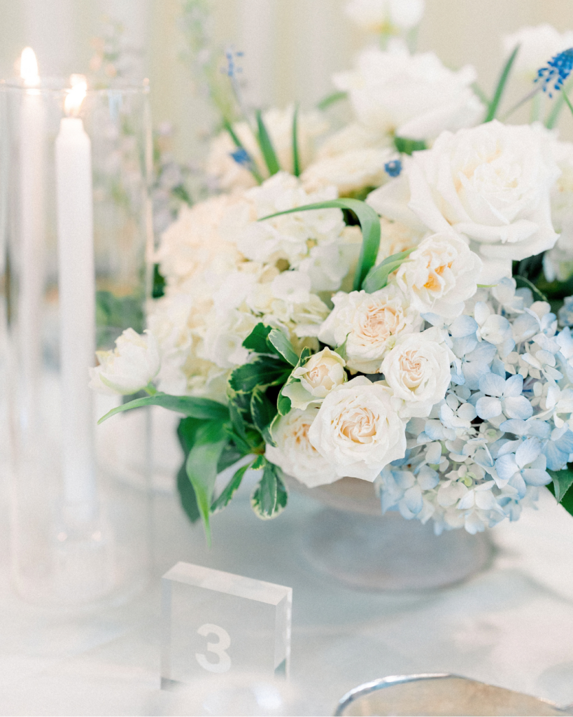 Close up of white roses, pale blue hydrangeas, greenery, and candlelight at the wedding reception.