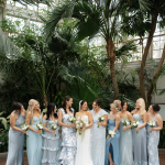 Bride and wedding party posing beneath palm trees inside a conservatory.