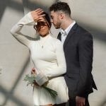 Couple standing close together in sunlight, with the bride shielding her eyes.