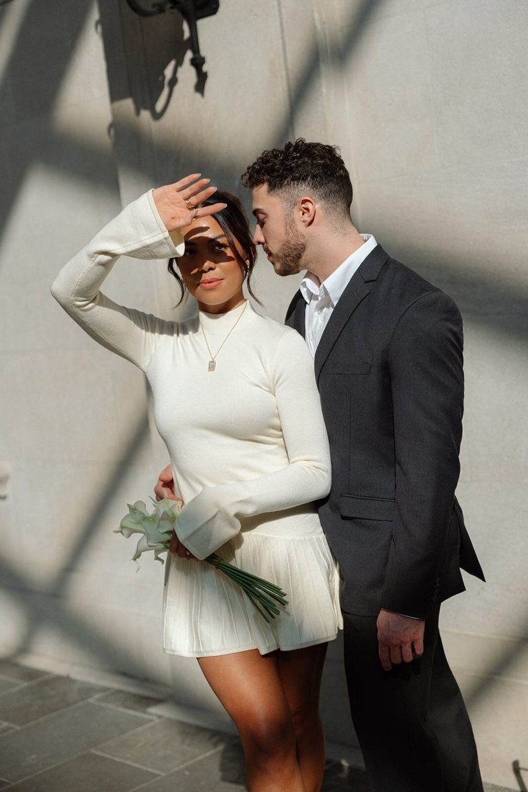 Couple standing close together in sunlight, with the bride shielding her eyes.