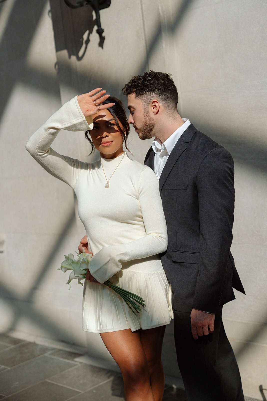 Couple standing close together in sunlight, with the bride shielding her eyes.