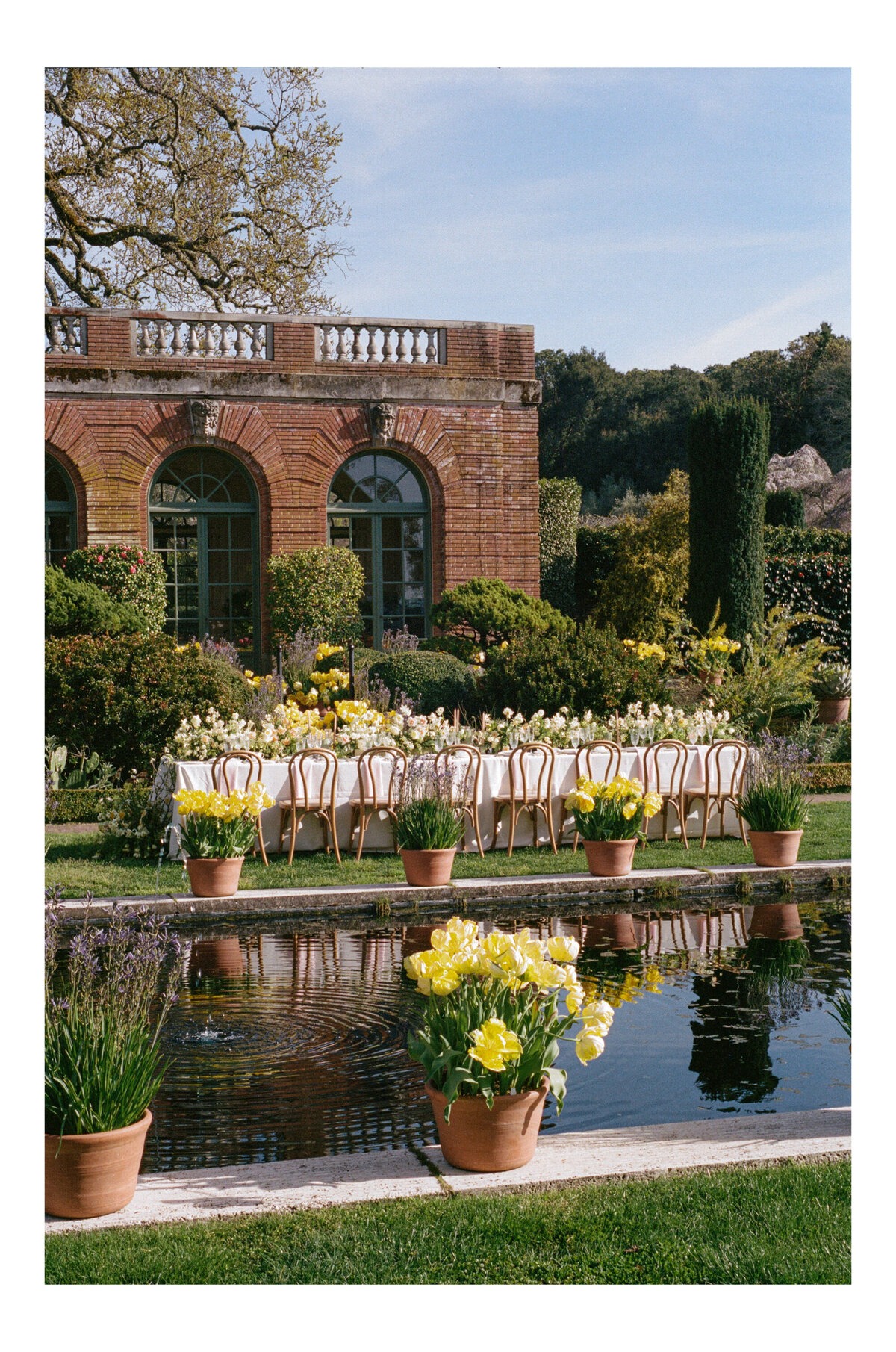 Outdoor wedding reception setup beside a reflecting pool and brick building.
