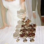Bride pouring champagne into a tower of coupe glasses.