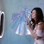 Two wedding guests pose with iridescent umbrellas in front of a Best Booths in Town ring-light photo booth.