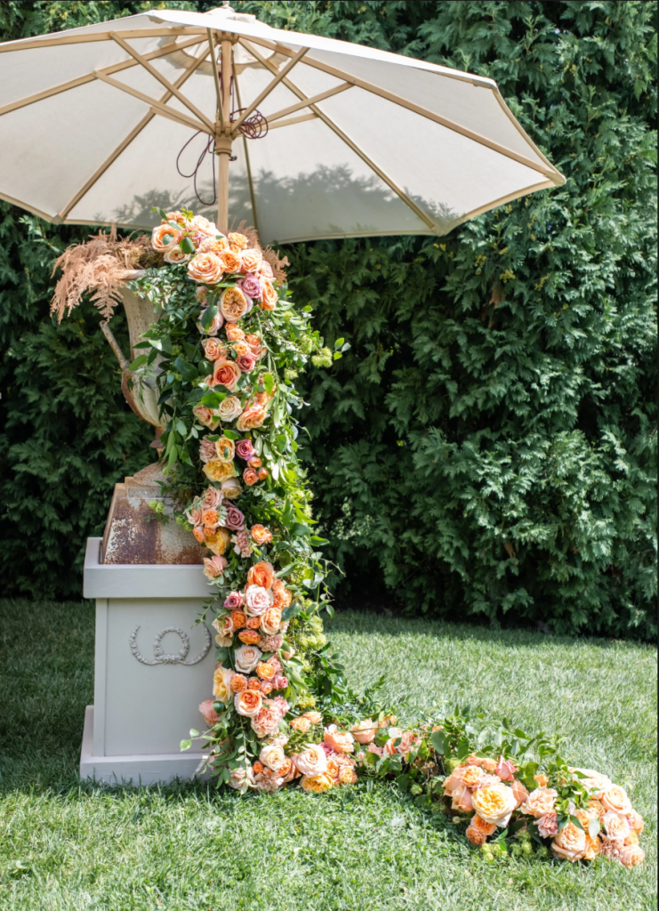 Cascading peach and blush rose wedding floral installation with greenery displayed outdoors beneath a white umbrella in Columbus, Ohio.