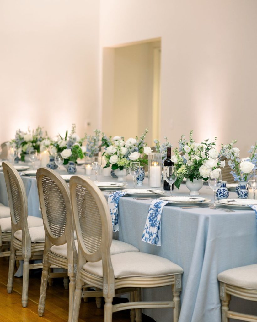 Pale blue table linens, blue patterned napkins, white floral arrangements, and cane back chairs.