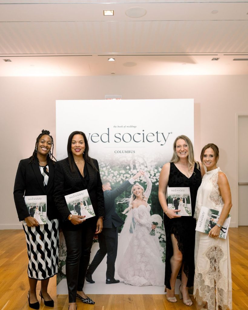 Four guests hold the Columbus Book of Weddings while posing in front of an oversized magazine cover display.