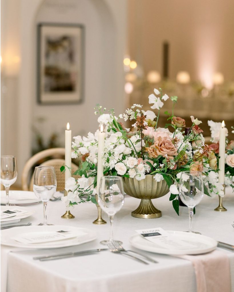 Blush and white floral centerpiece in a green footed vase with taper candles and white place settings.