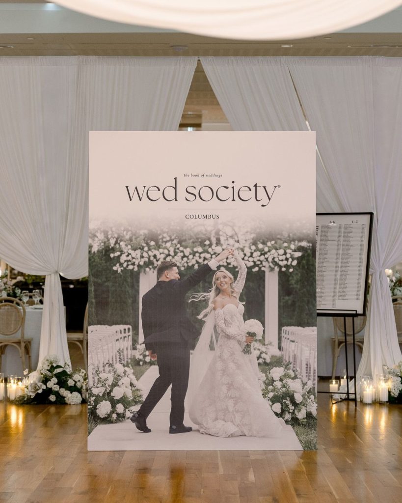 Oversized 2026 Wed Society Columbus magazine cover displayed in front of white draping and candles.
