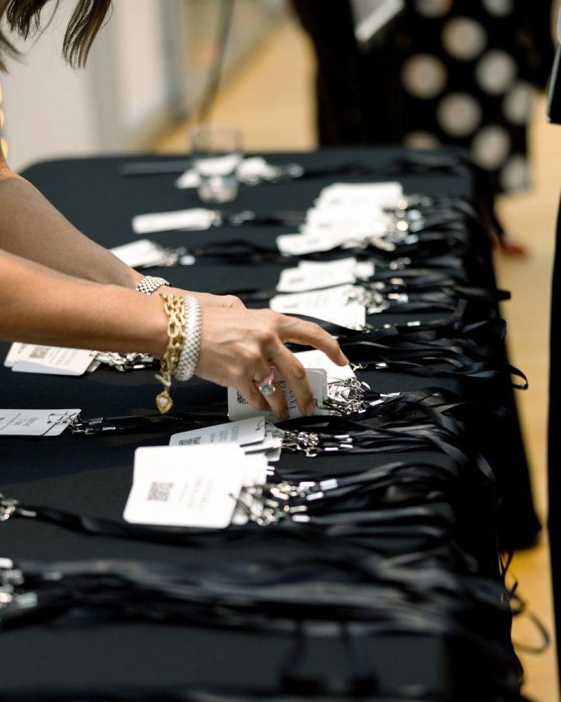 Guest reaches for a name badge among rows of black lanyards at the event check in table.