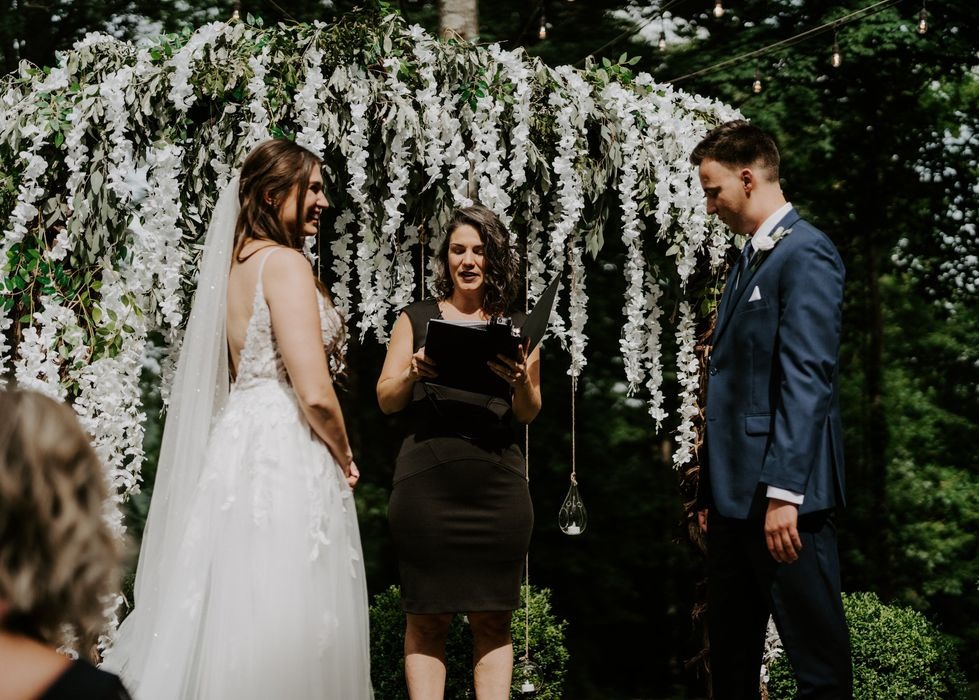 Bride and groom exchange vows with a Columbus wedding officiant beneath a white floral ceremony arch.