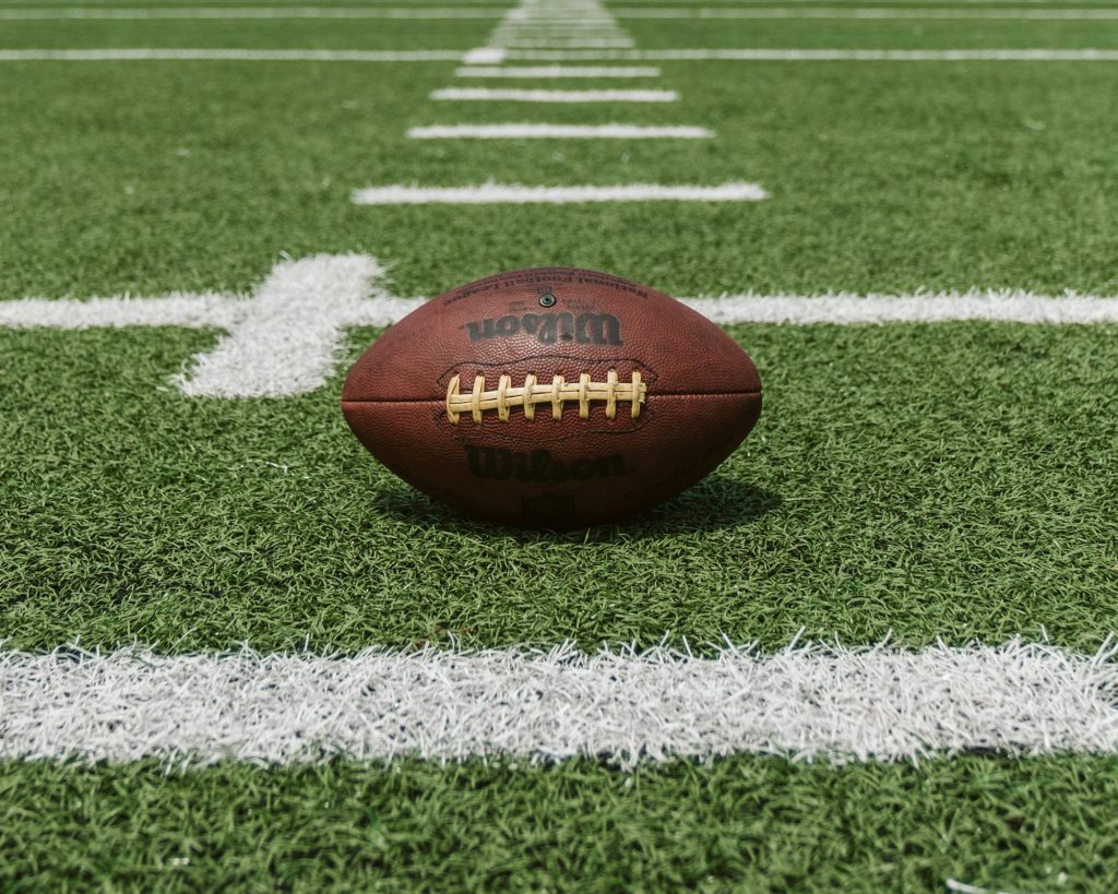 A Wilson football rests on green turf between white yard lines at Ohio Stadium.