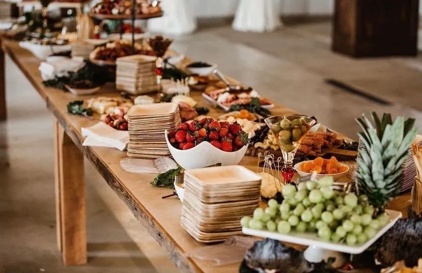 Wedding catering grazing table featuring fresh strawberries, grapes, pineapple, olives, cheeses and assorted appetizers arranged for guests.