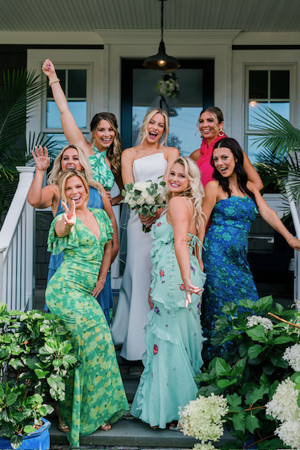 Bride and bridesmaids pose excitedly on the front steps of a house.