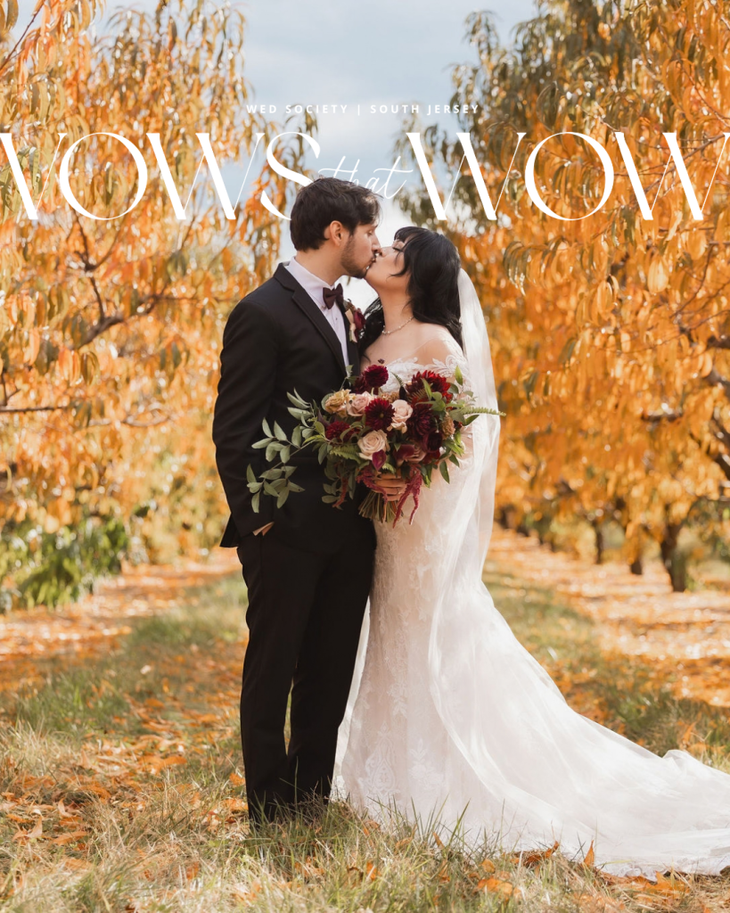 Bride in a white gown and long veil holds a large burgundy bouquet while standing close to the groom in a black suit among yellow autumn trees.