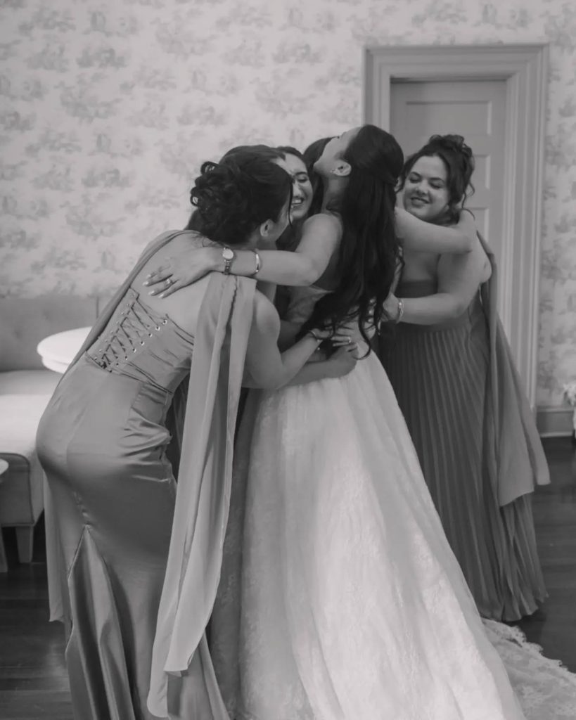 black and white photo of bride hugging bridesmaids at estate manor before wedding ceremony leesburg virginia