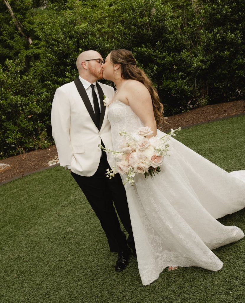 Bride and groom kissing on the lawn at Carolina Grove, groom in a white tuxedo jacket