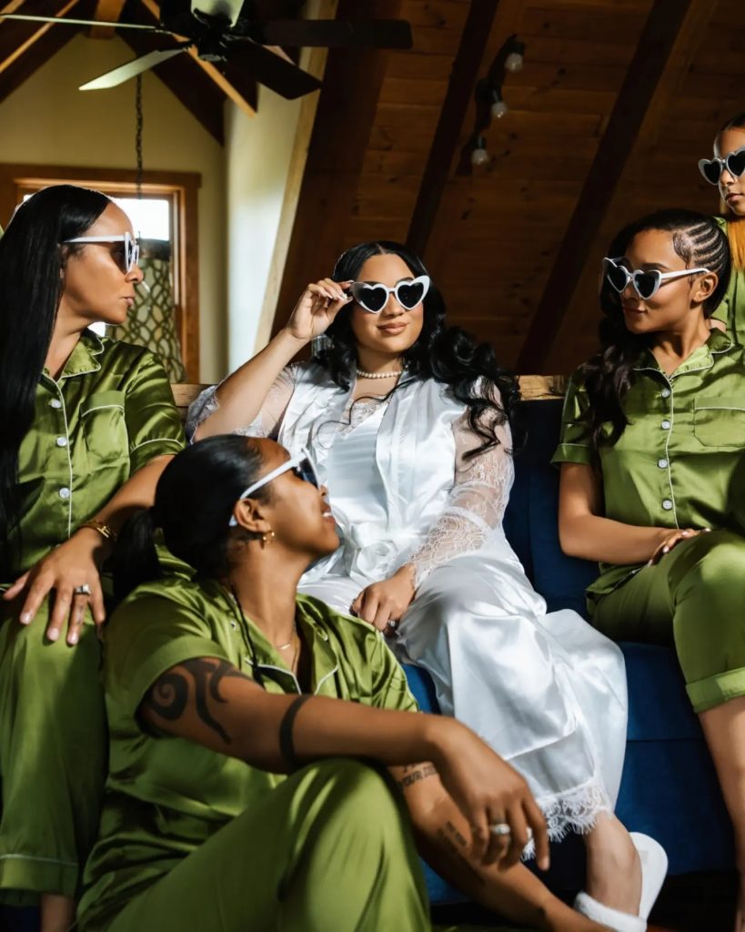 bride and bridesmaid in pajamas during getting ready photos wedding morning. bridesmaids in sage green silk pajamas and bride in matching white pjs