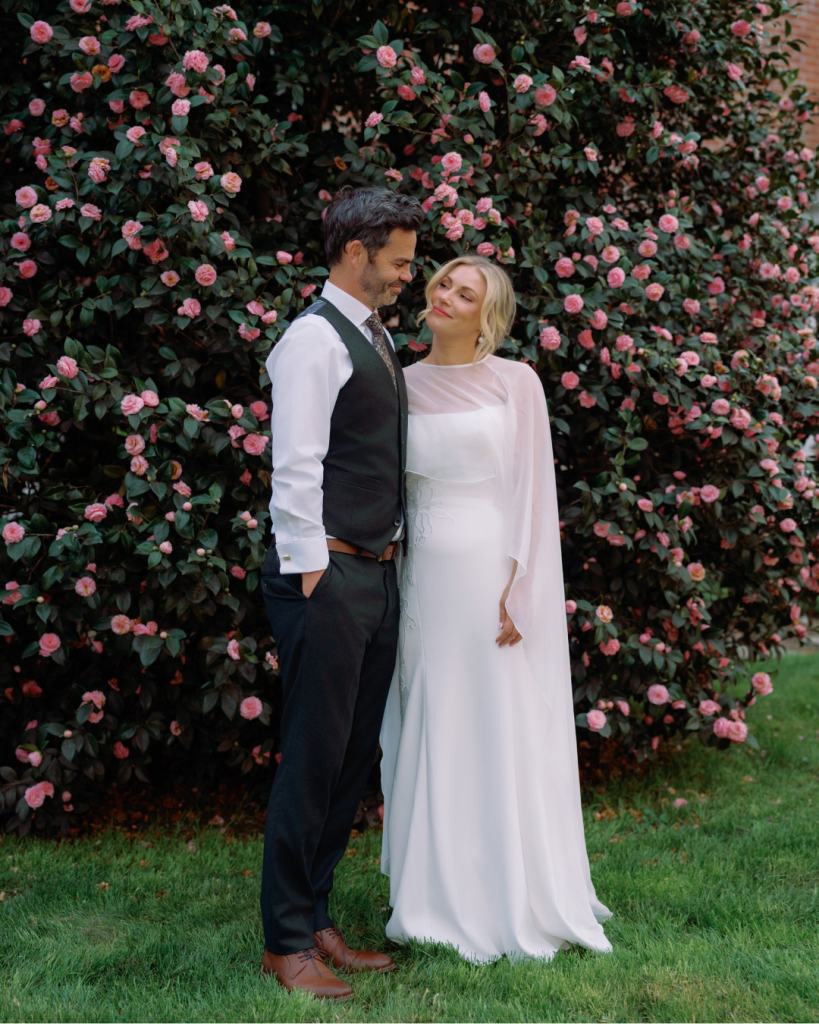 Elizabeth and Tom pose in front of blooming pink camellias during their garden party wedding at The Morehead Inn in Charlotte, NC.