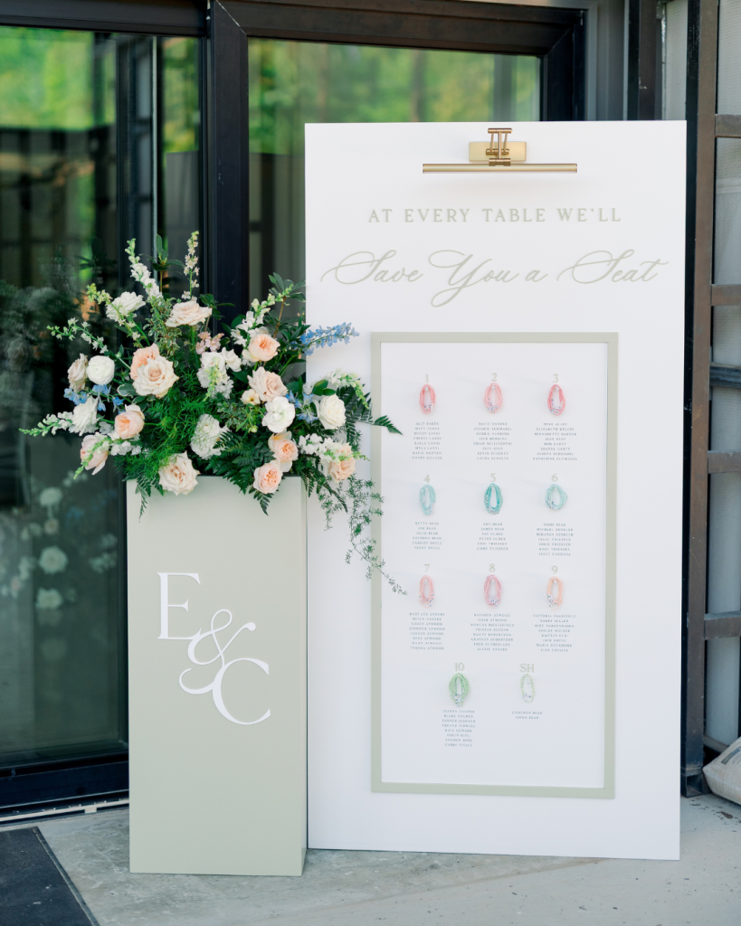 Custom friendship bracelet seating chart with peach and white florals at Emma and Cameron’s wedding at Splendor Pond in Mooresville, North Carolina.