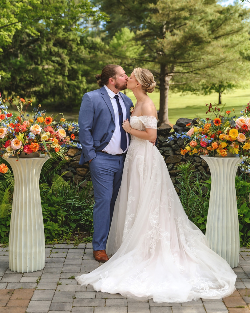 bride and groom outdoors during their garden wedding, framed by colorful floral arrangements and lush greenery.